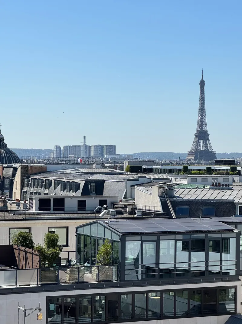 Paris rooftops under a clear sky, with the Eiffel Tower on the horizon